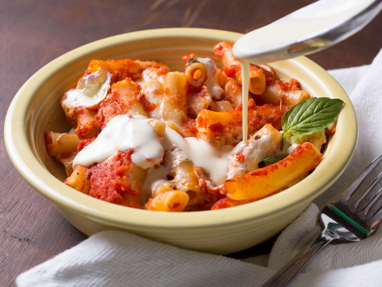Bowl of baked ziti drizzled with Parmesan cream.