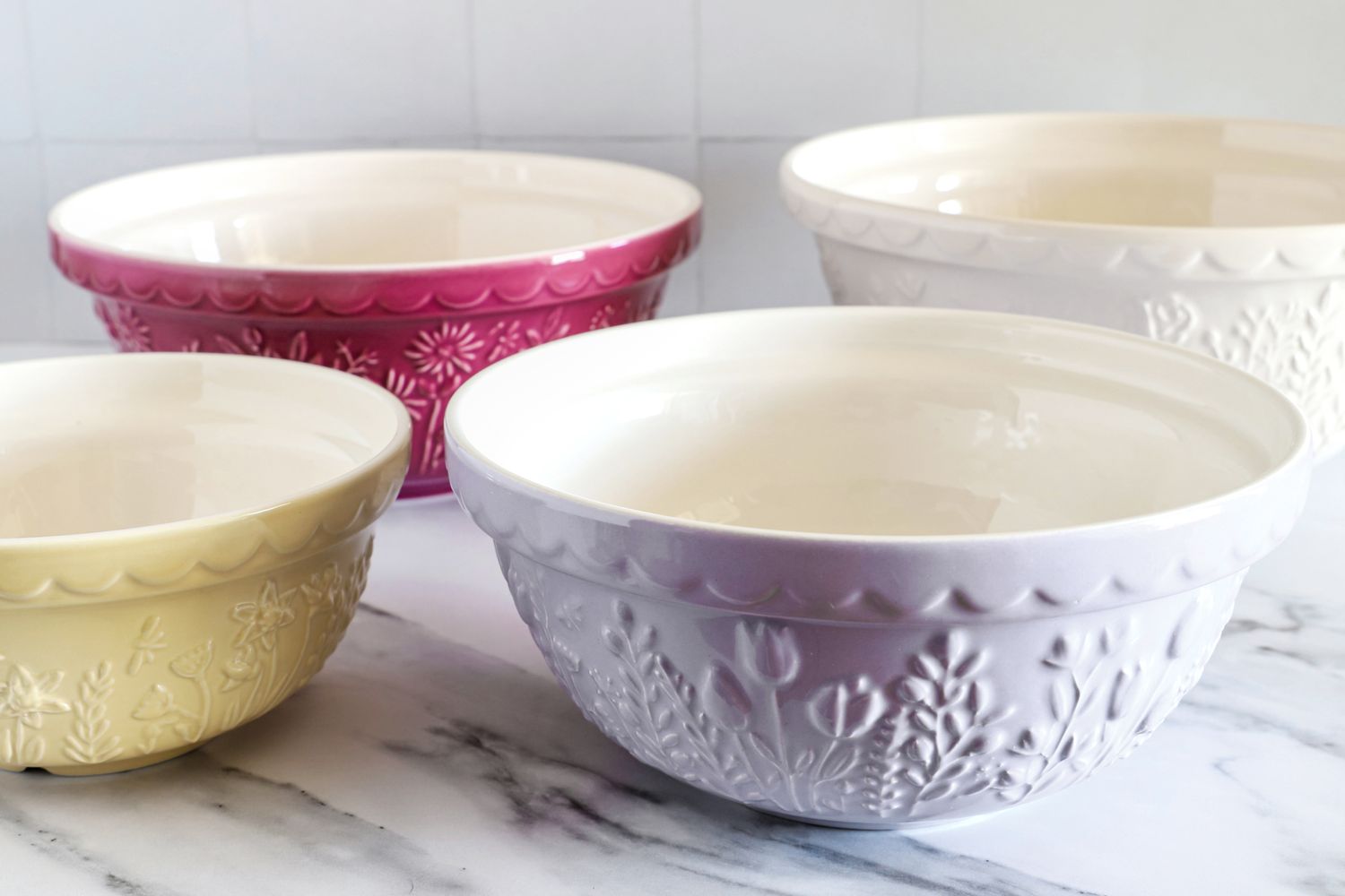 Four Mason Cash ceramic mixing bowls with floral designs arranged on a marble surface
