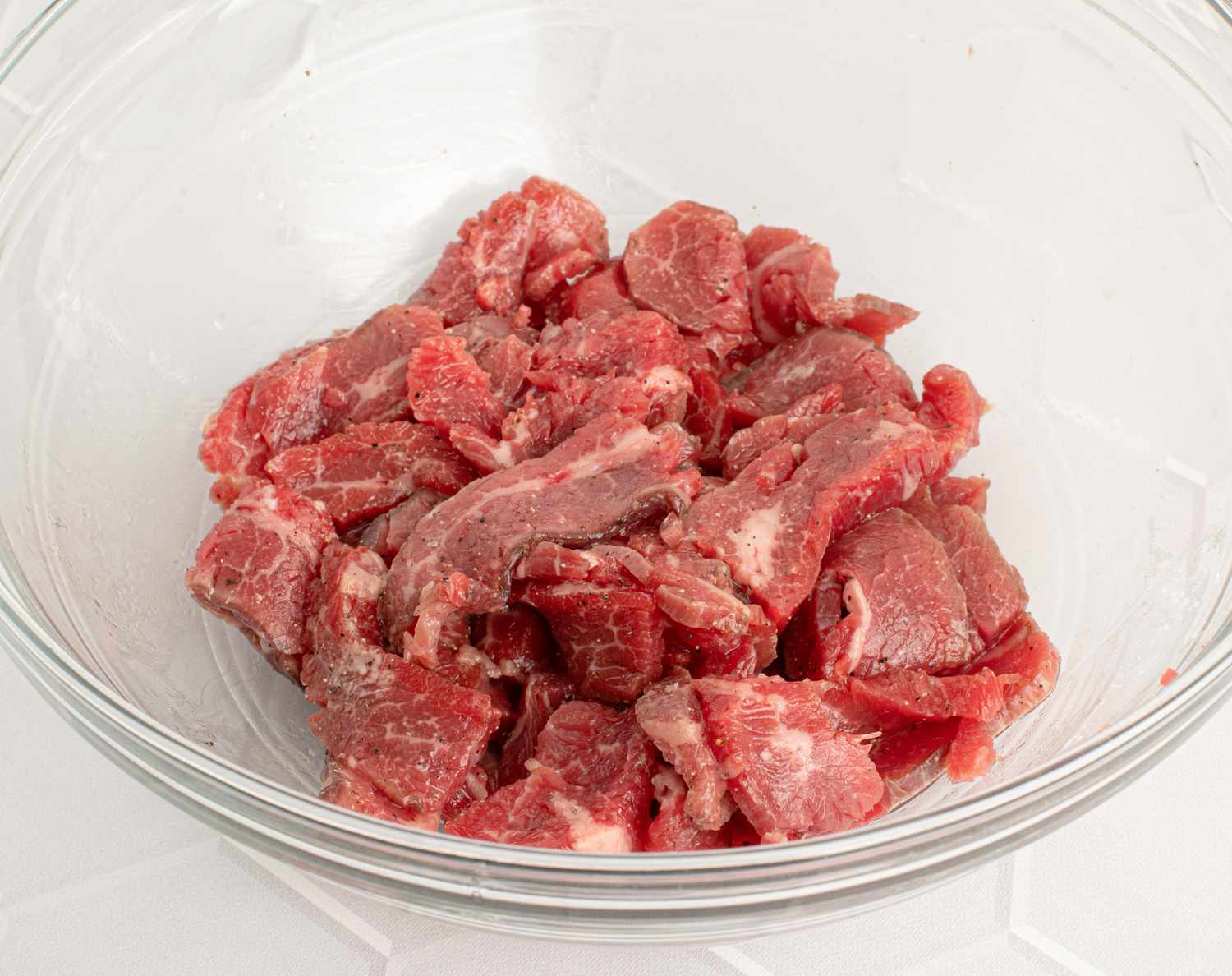 Beef, salt, sugar, ground black pepper, Shaoxing wine, Â½ teaspoon soy sauce, 1 teaspoon oil, and cornstarch mixed well inside a glass bowl. The beef is coated in a thin film, showing all the ingredients have mixed together.