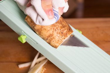 Closeup of a potato being sliced with a mandoline.