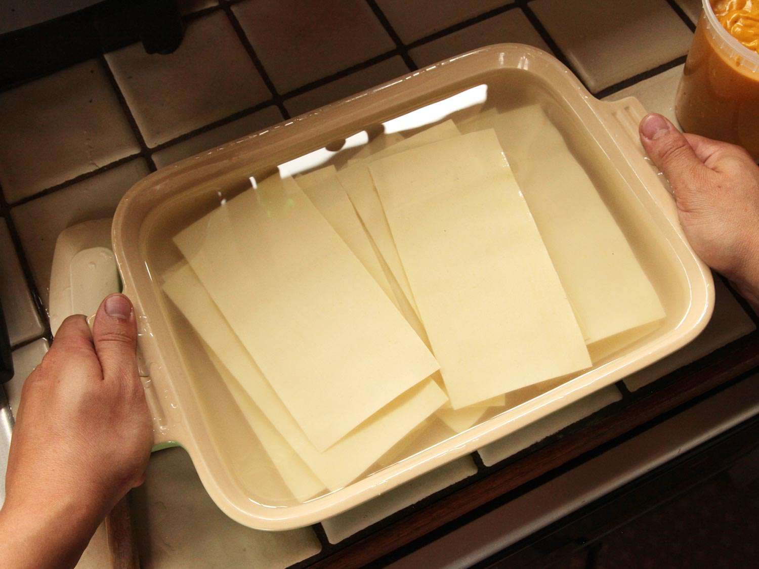 Lasagna sheets soaking in baking dish of water.