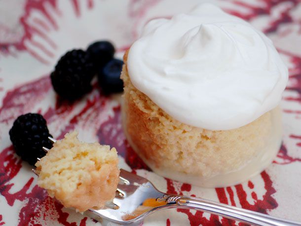 Closeup of a round portion of tres leches cake. A bite of cake is suspended nearby on the tines of a fork.