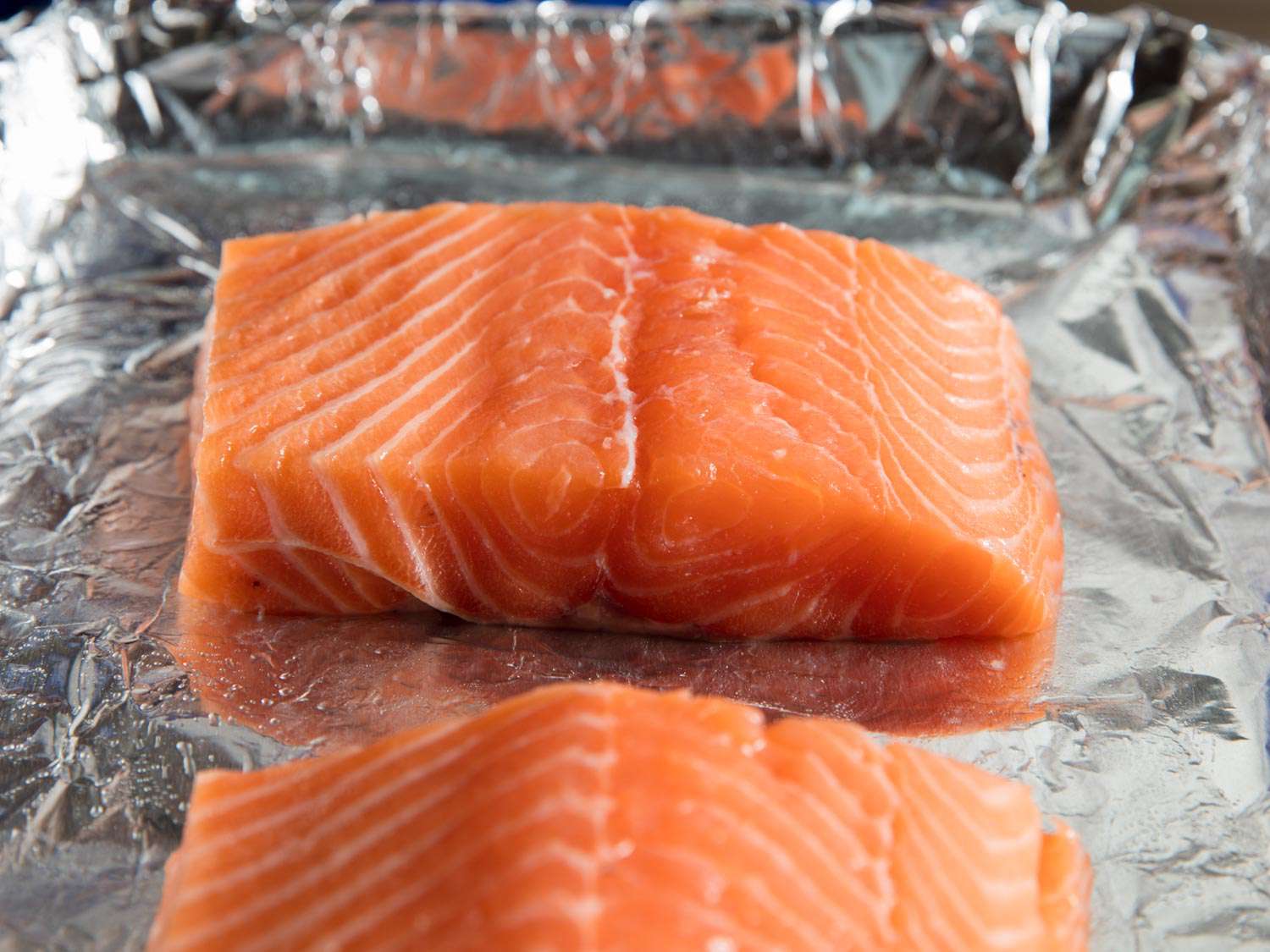 Two similar sized salmon pieces on a tray lined with aluminum foil.