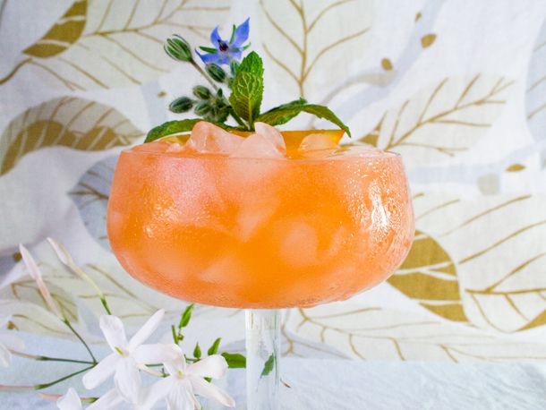 Cocktail in glass garnished with mint, in front of leaf-printed fabric background.