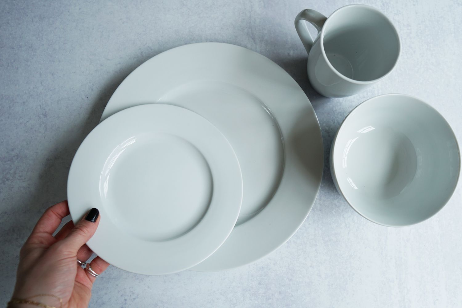 A hand placing a white salad plate onto a white dinner plate