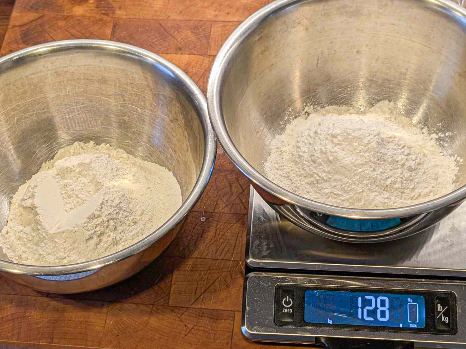 Two bowls containing flour with one bowl placed on a digital kitchen scale showing a weight of 128 grams