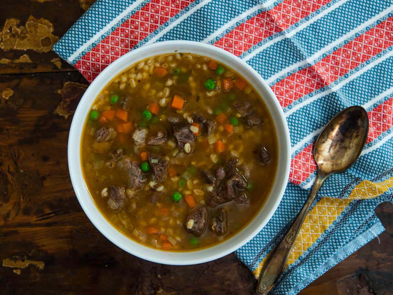 Overhead shot of bowl of beef barley vegetable soup and a spoon next to it. 