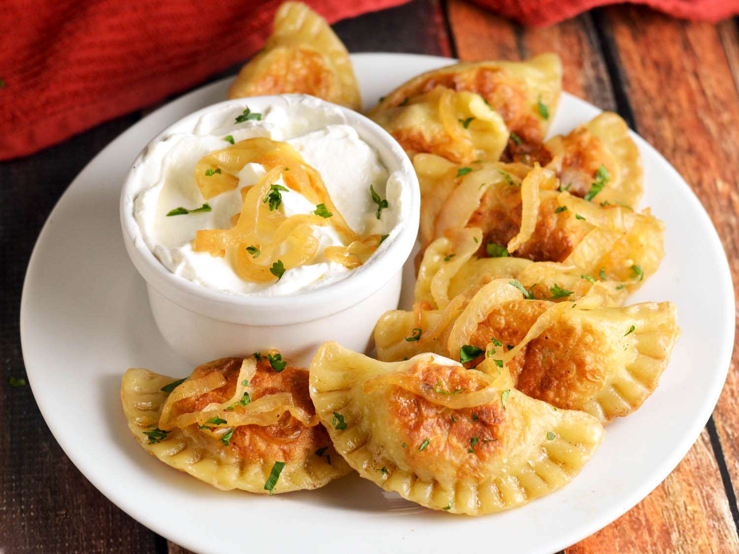 plate of onion-topped cheesesteak pierogi with ramekin of sour cream