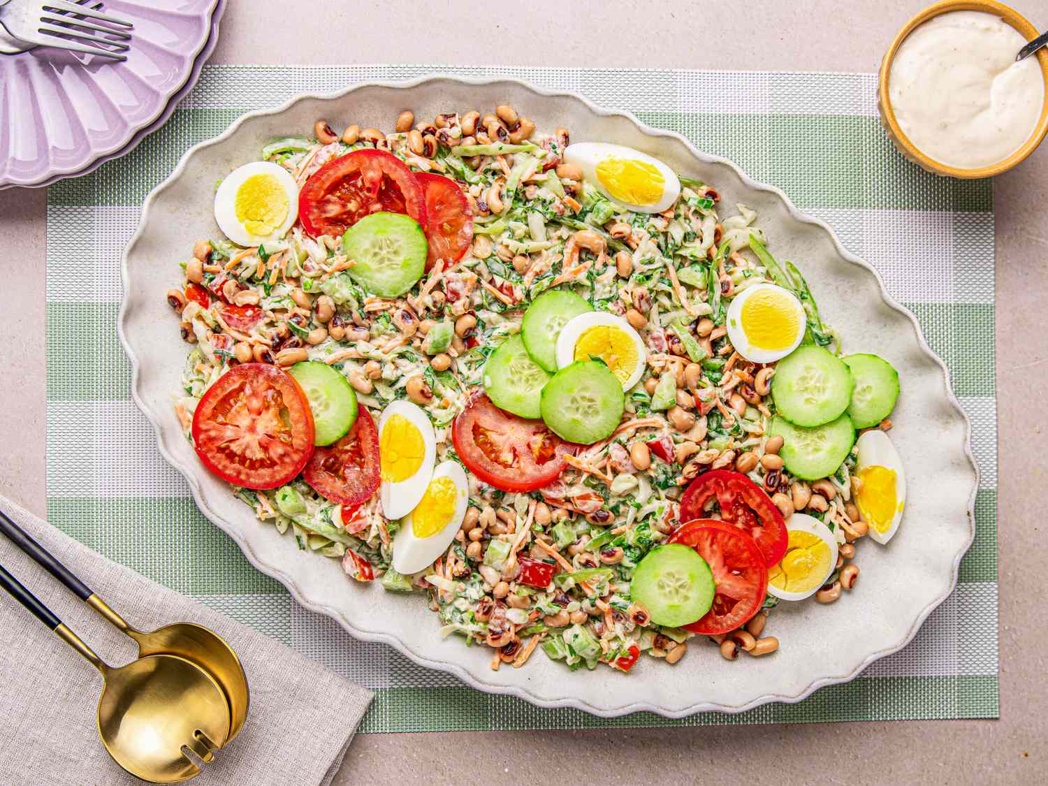 A serving dish with Nigerian salad containing sliced tomatoes cucumbers boiled eggs and beans on a checkered tablecloth