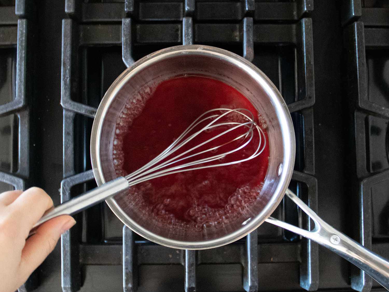 Pomegranate juice and sugar being whisked together in a saucepan