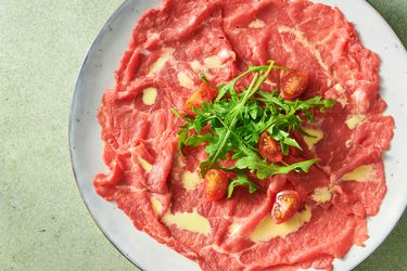 beef carpaccio garnished with tomato quarters and baby arugula