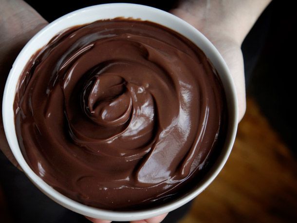 A bowl of pudding behind held by two hands.