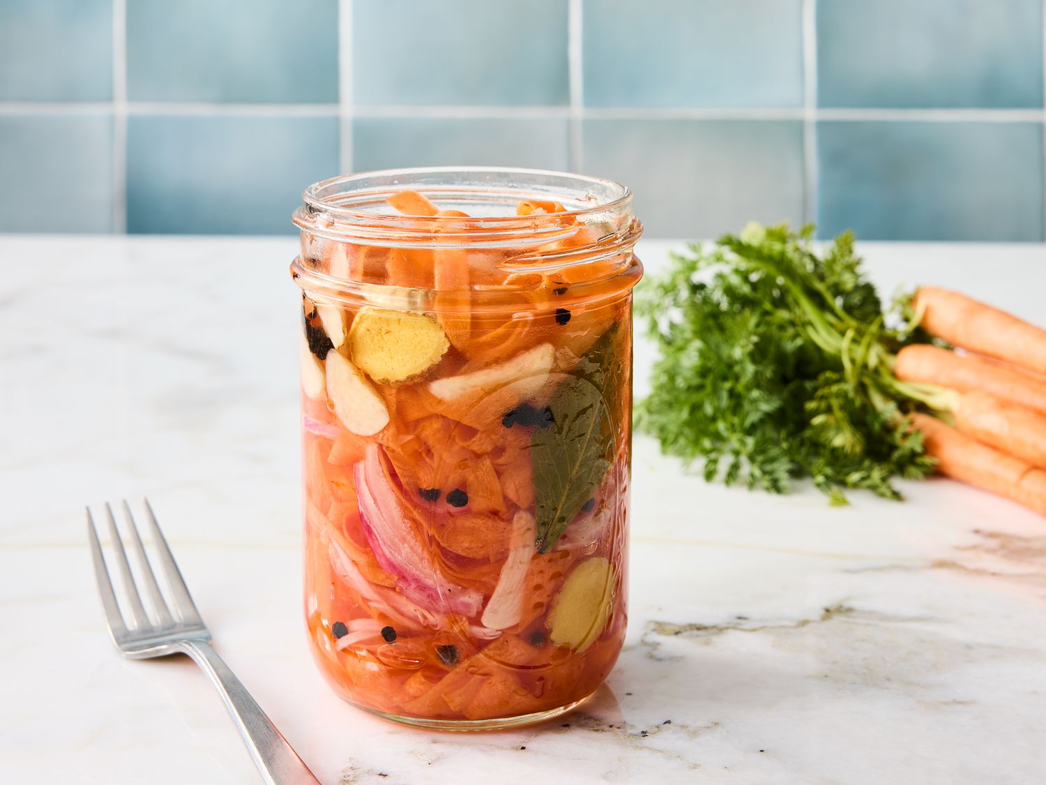 carrot ribbons in a jar with a fork on the side, with blue tile backsplash