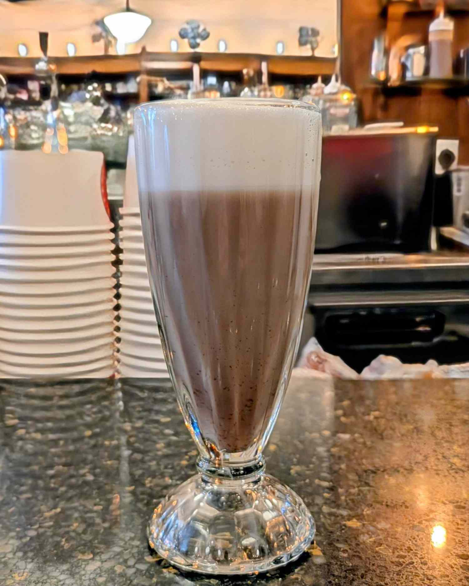 A glass of egg cream on a counter in a cafe setting