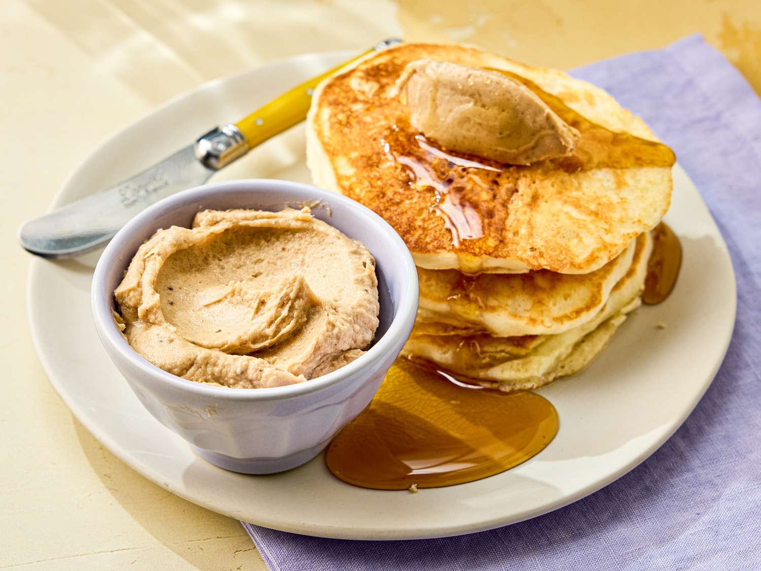 Pancakes served with a bowl of banana butter and syrup on a plate