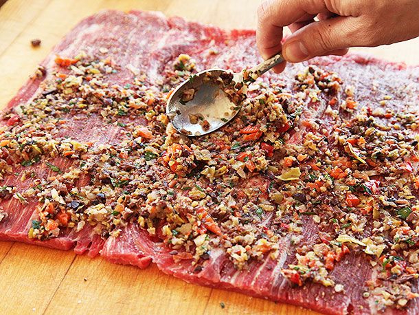 Spreading chopped olive salad with spoon over butterflied piece of flank steak