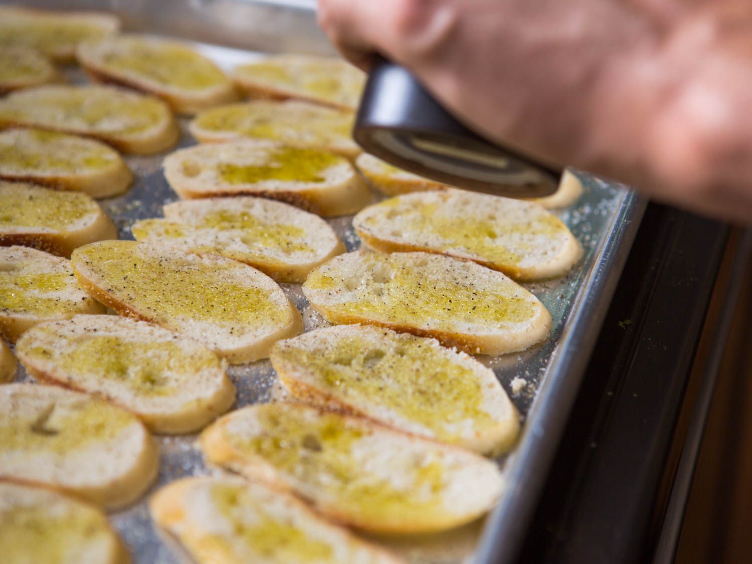 Seasoning baguette slices with salt and pepper for homemade baguette toast crackers