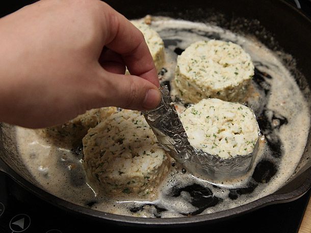 A hand taking foil off a crab cake frying in butter. 