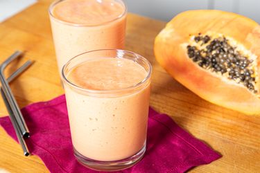 Two glasses of fruit smoothie next to half a papaya on a table