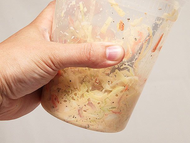 Hand holding a container of soggy, soupy coleslaw in a quart-sized deli container
