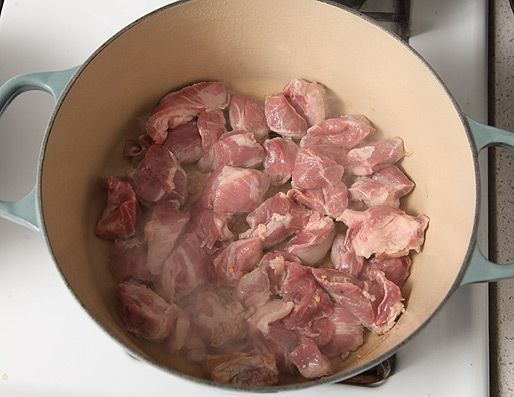 An enamel cast-iron Dutch oven with pieces of pork shoulder in a single layer on the bottom of the pot. 