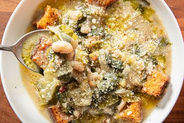 A bowl of zuppetta Scarola e Fagioli with croutons and beans a spoon scooping out the soup