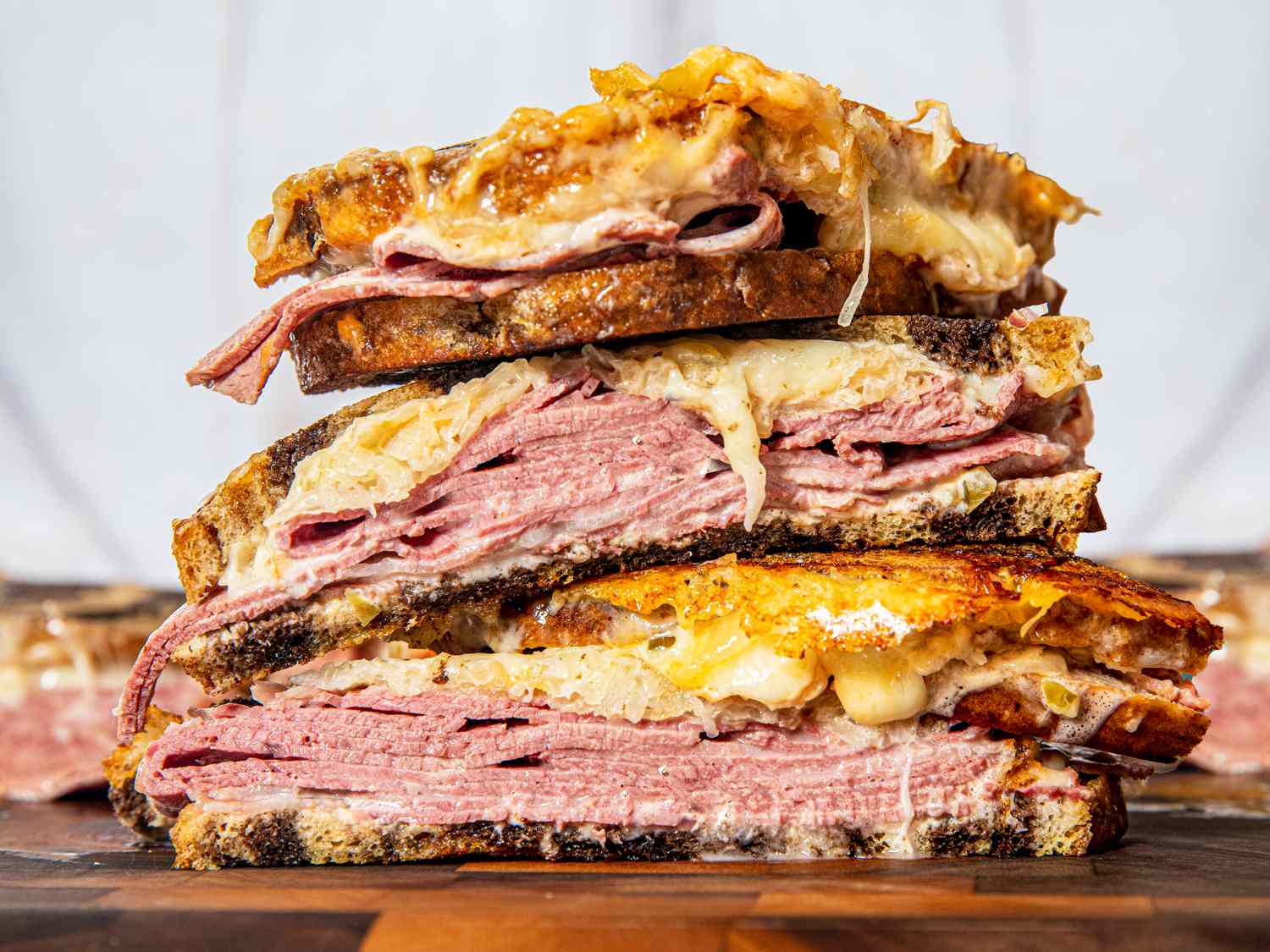 Three reuben sandwich halves stacked on top of each other on a cutting board
