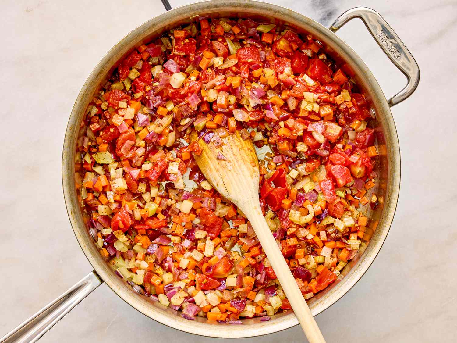 A pot containing diced vegetables being cooked with a wooden spoon resting inside