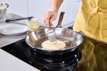A person pouring crepe batter into a stainless steel skillet