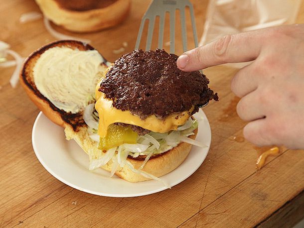 Smash cheeseburger being transferred onto dressed burger bun 