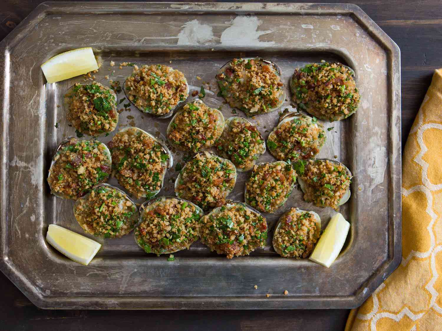 A tray of baked clams casino garnished with lemon wedges