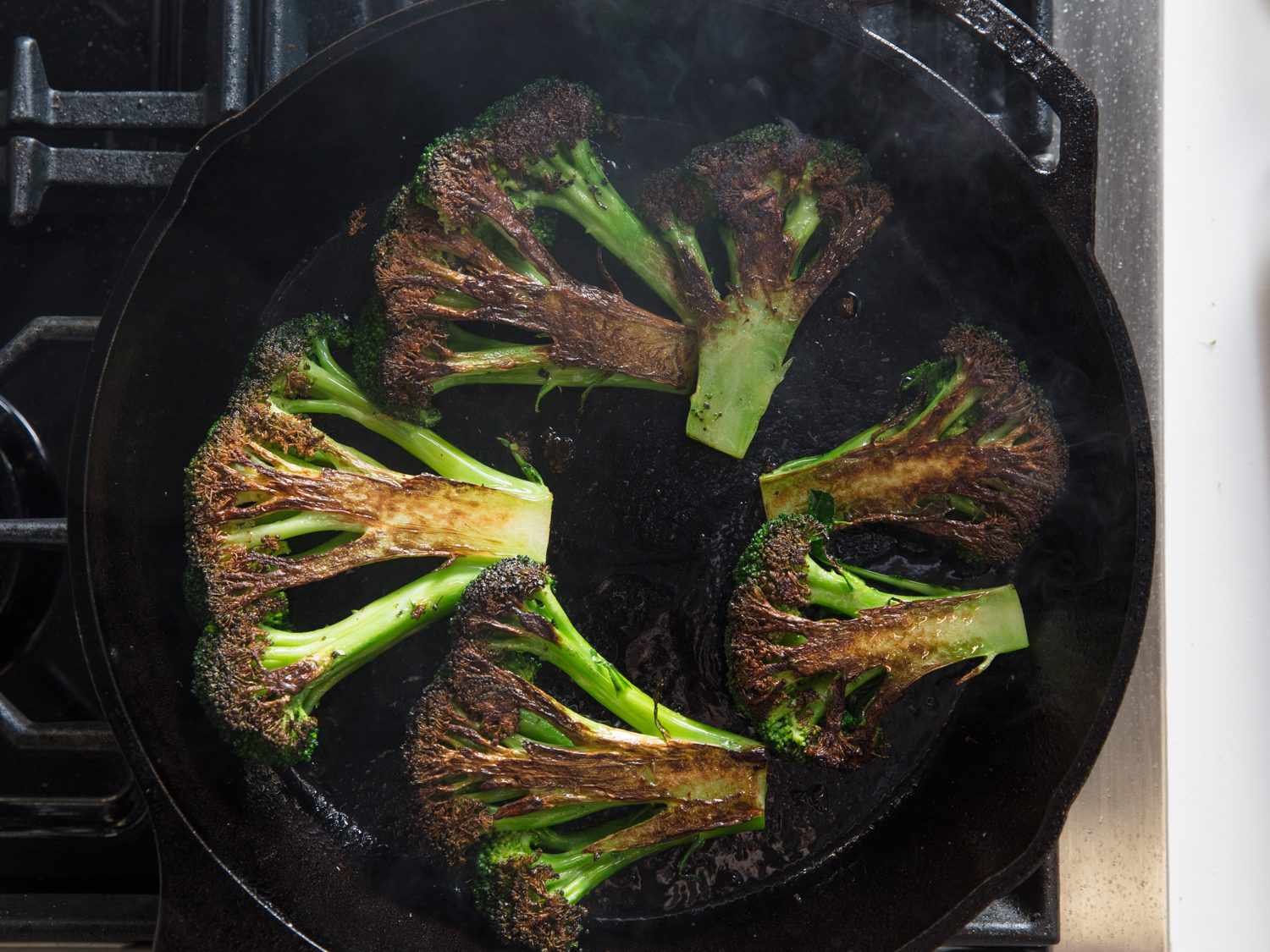 Overhead shot of charred broccoli pieces cooking in a cast iron skillet.