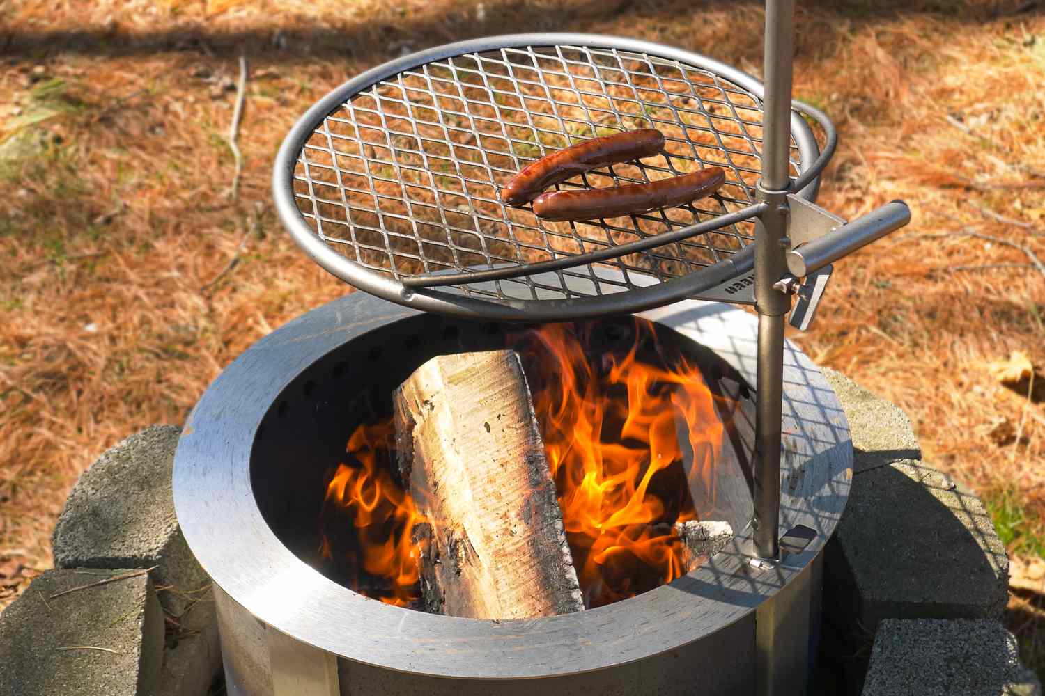 Hot dogs cooking on a grill over a flaming outdoor firepit