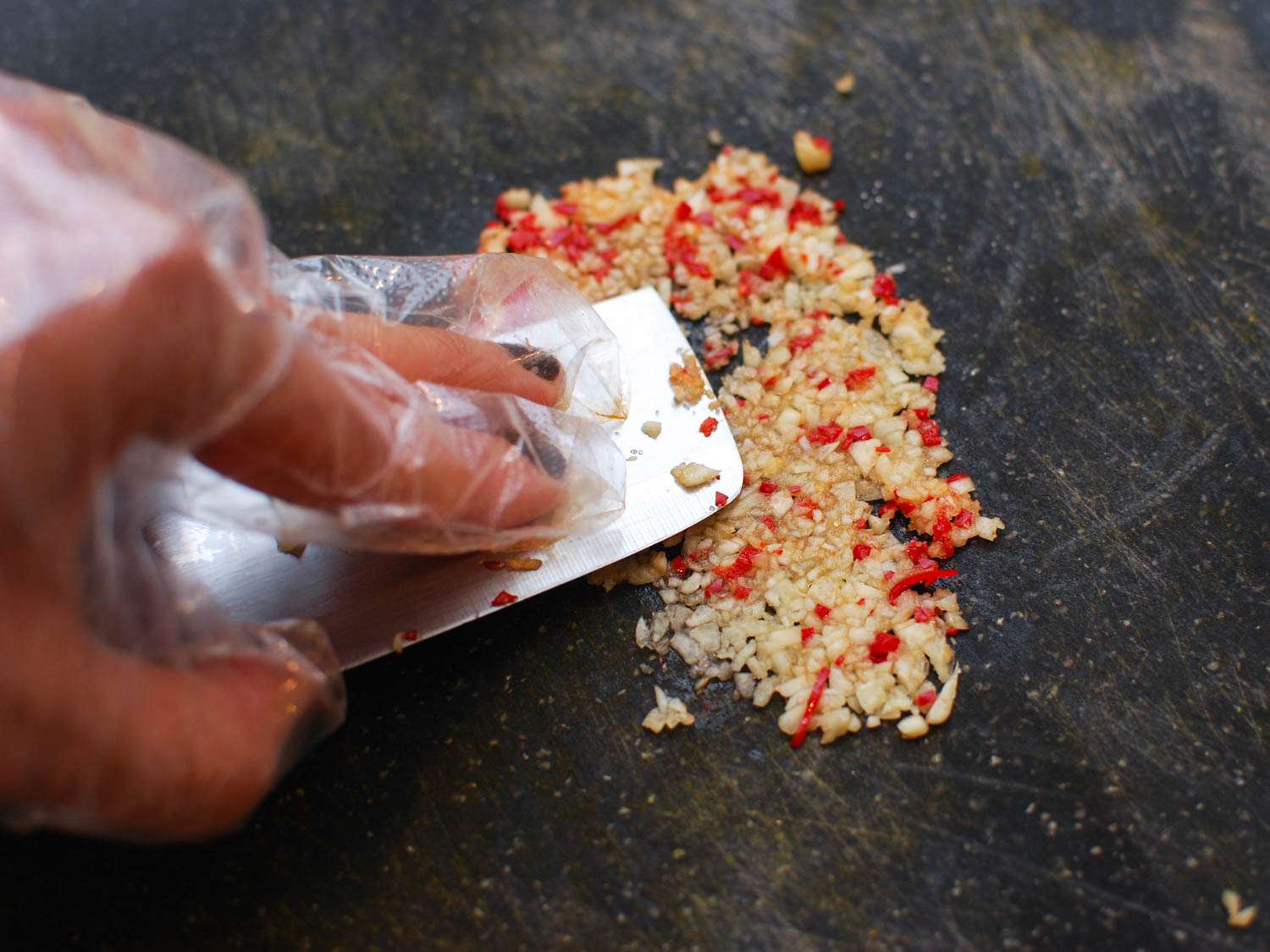 Working garlic and red chiles into a paste with the side of a knife.