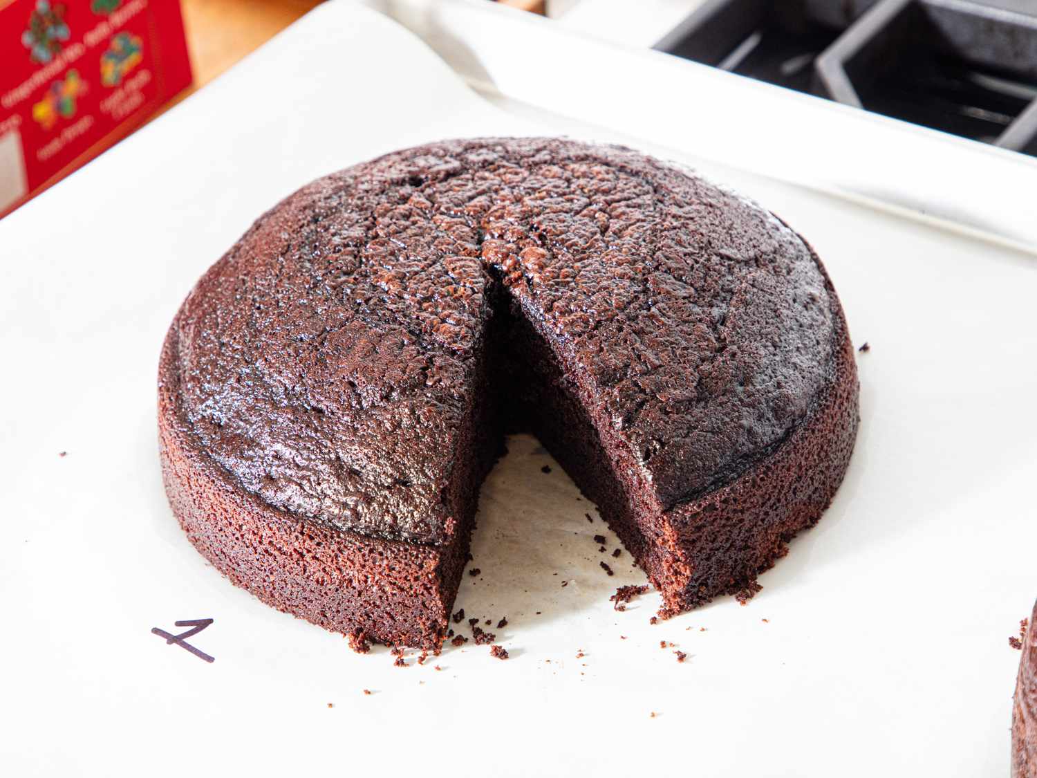 A round chocolate cake with a slice removed placed on a white surface