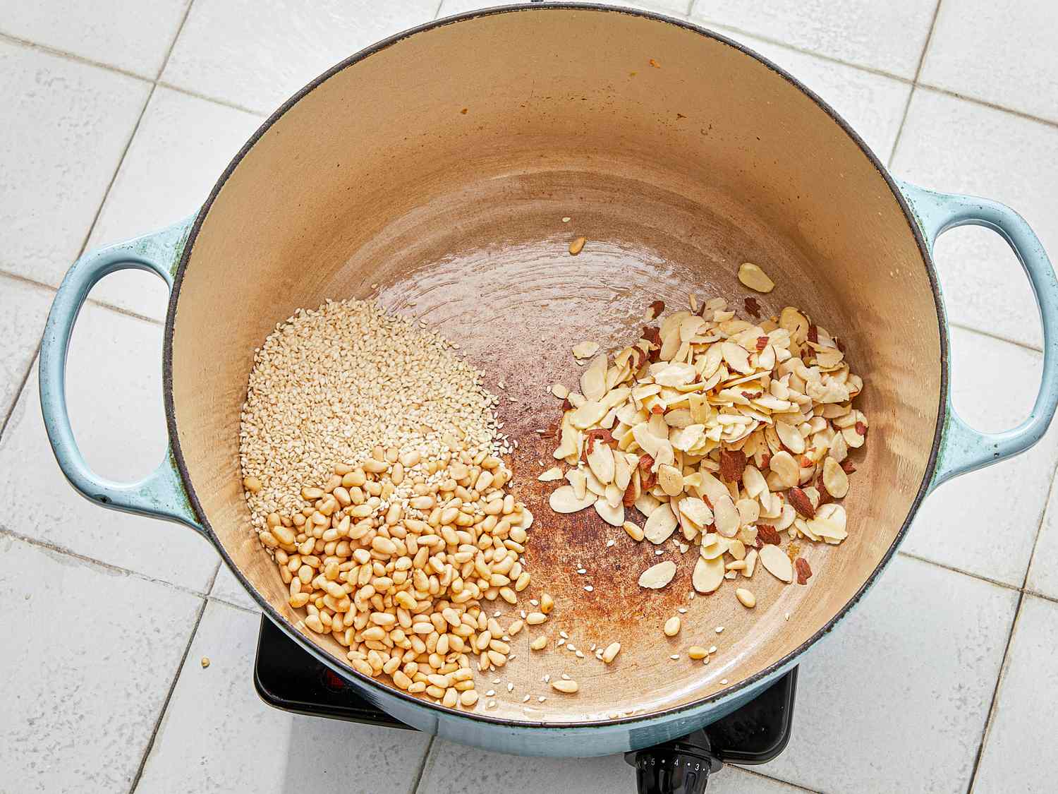 Sesame seeds and sliced almonds being roasted in a pot on a stovetop