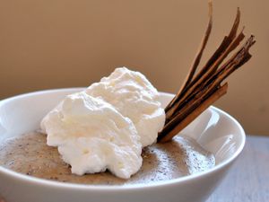 Closeup of cinnamon-orange pudding, served in a small white bowl with a slivered canela cinnamon garnish and whipped cream.