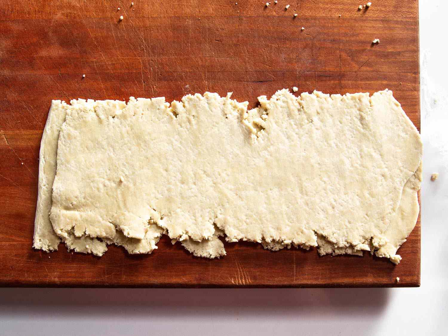 Two sheet-like things of very crumbly aspect place one on top of the other, in preparation for rolling through pasta rollers