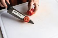 A person using a knife to slice a tomato