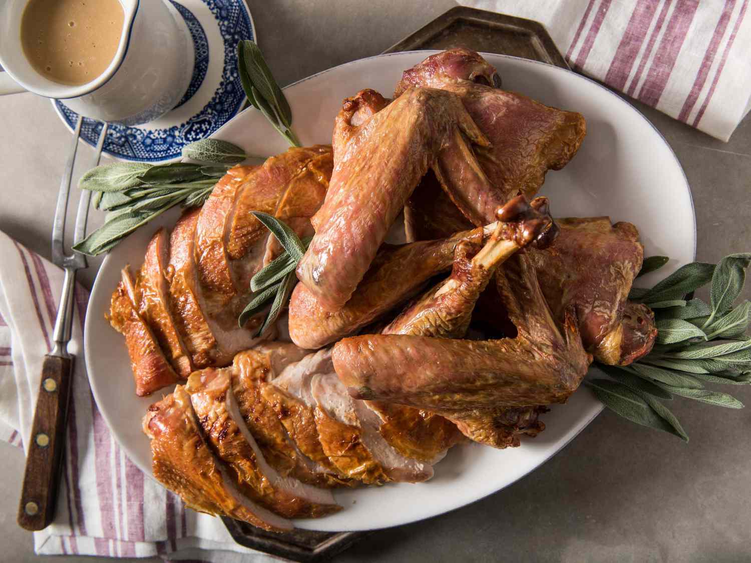 Roasted, carved turkey on a platter with sage leaves. A pitcher of gravy is next to the platter.