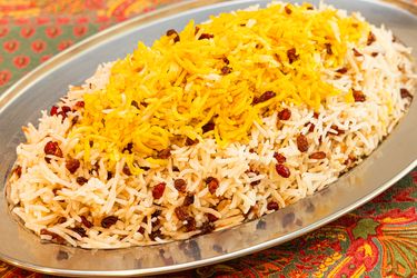 A dish of rice topped with barberries served on a metal platter placed on a patterned tablecloth