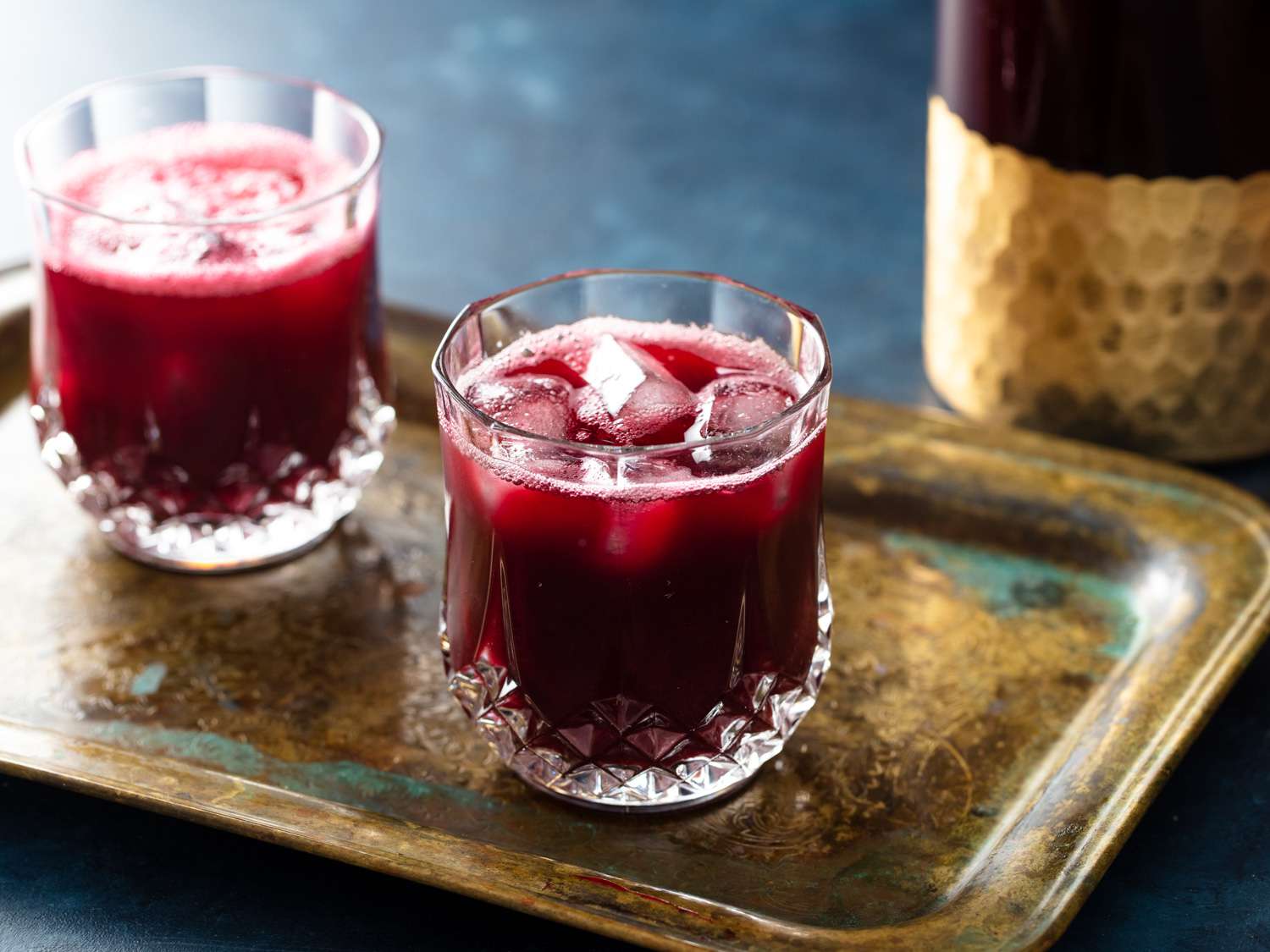 Two glasses of Jamaican sorrel hibiscus drinks resting on an old copper platter.