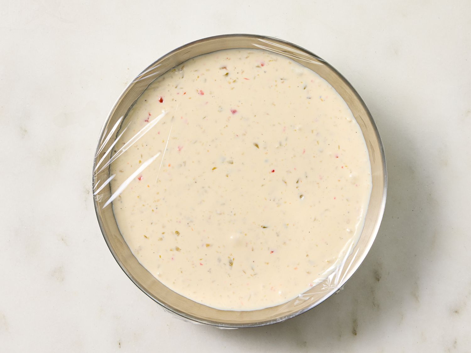 A bowl of creamy dip covered with plastic wrap