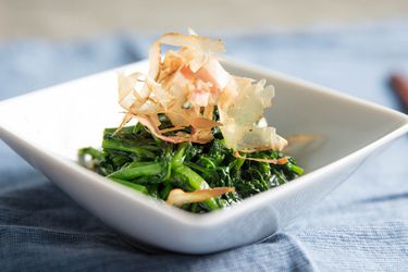 Side view of a dish of ohitashi topped with shaved bonito