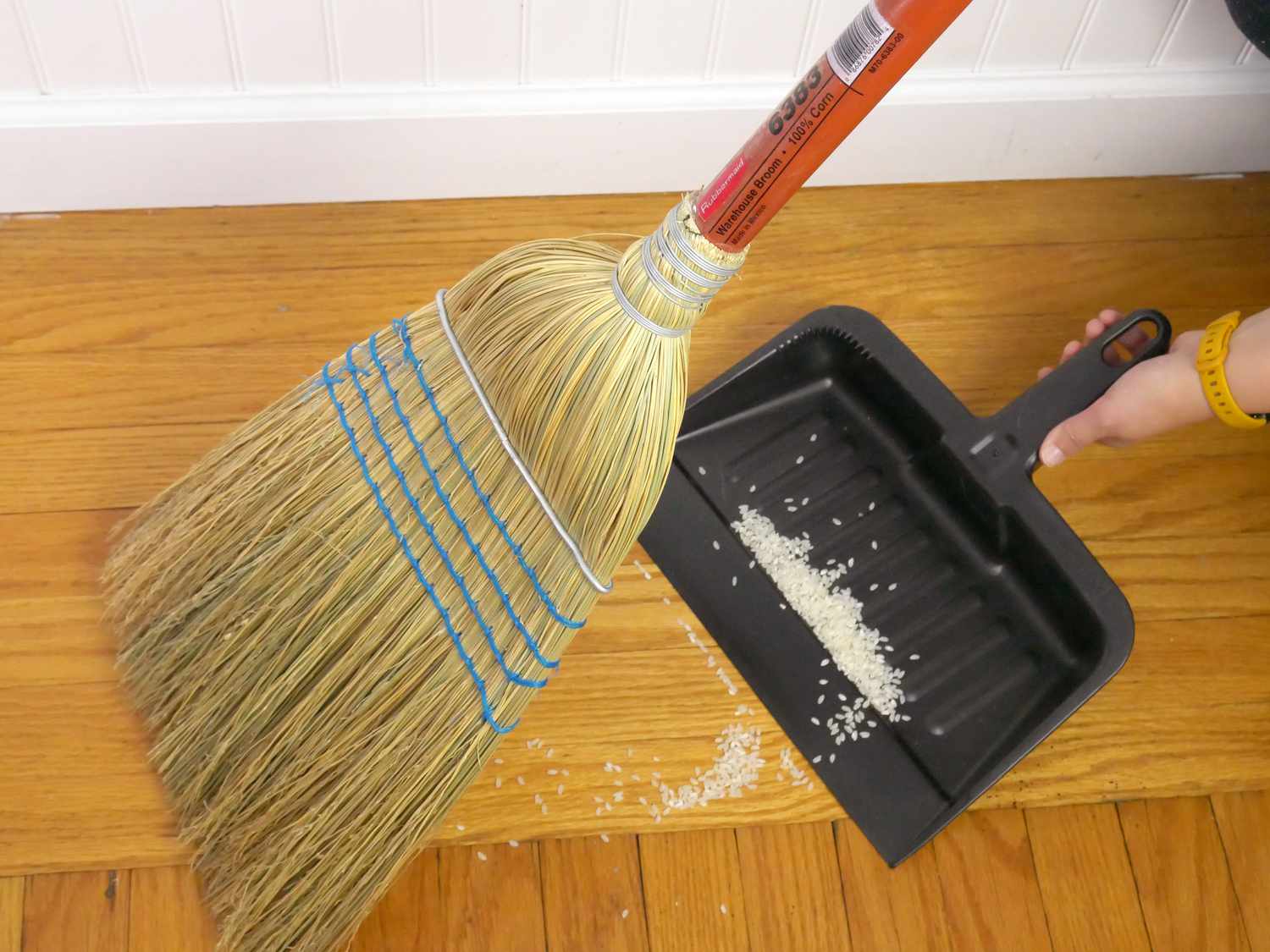 a person using the rubbermaid corn broom to sweep rice into a dustpan