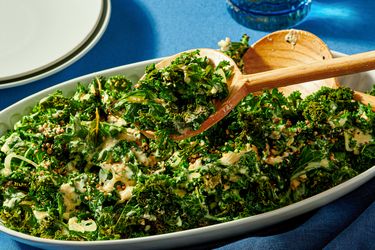 A dish of roasted kale salad with wooden serving spoons on a blue tablecloth