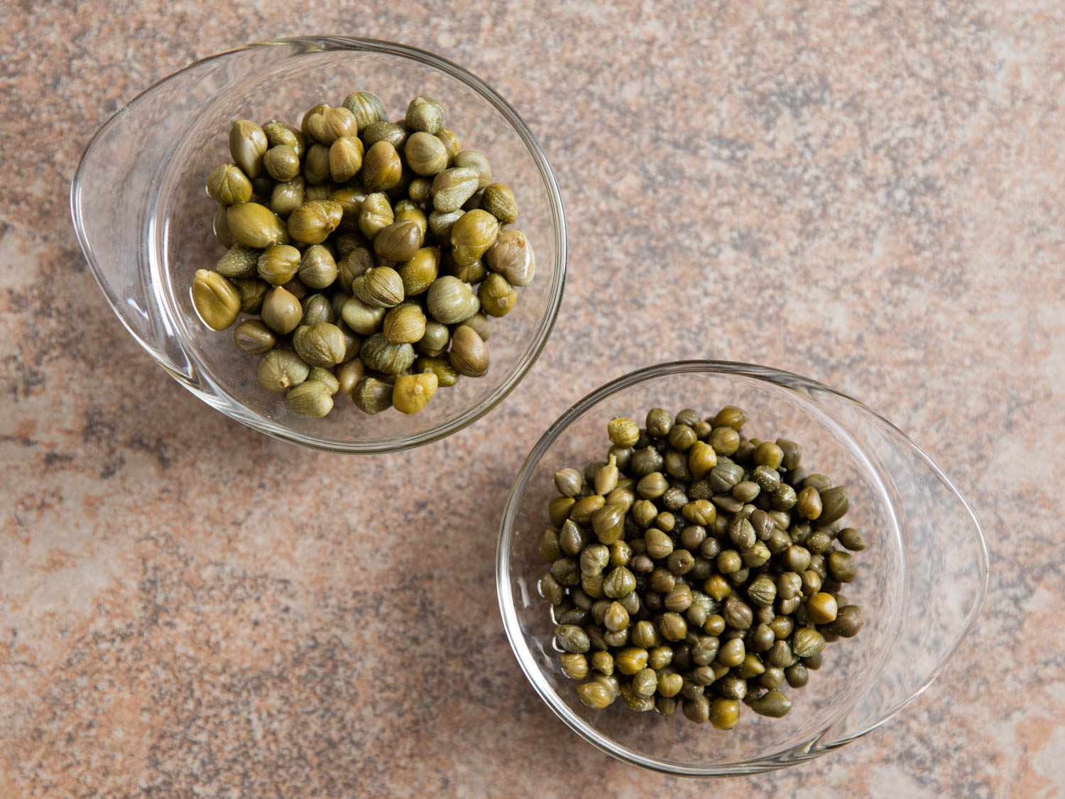 Two small bowls of different sized capers. 