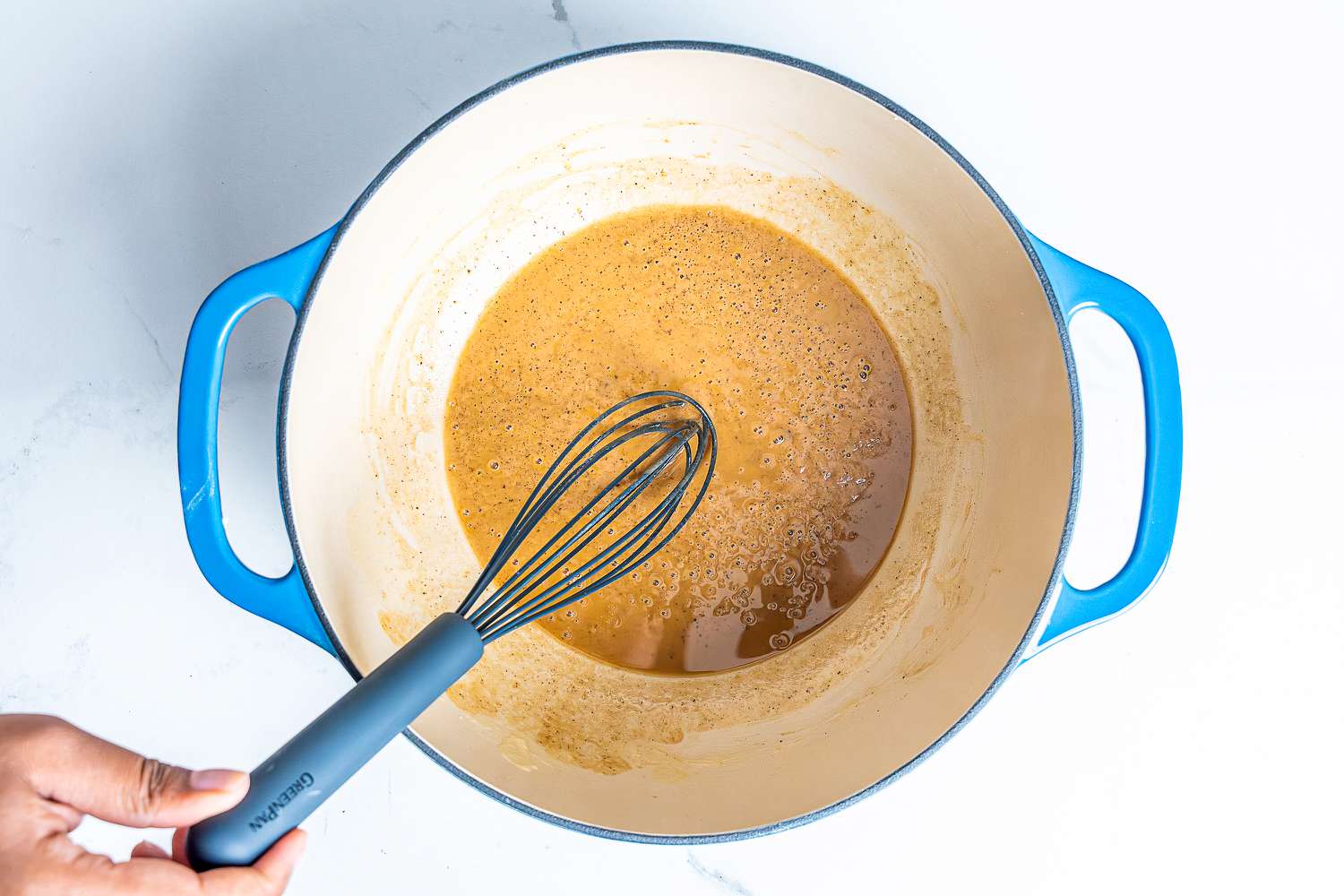 A hand holding the GreenPan Silicone Whisk in a pot