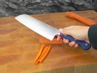 a person holding the wusthof knife over a cutting board with sliced carrots