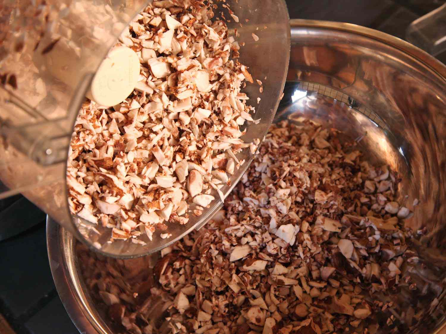 Chopped mushrooms inside of a food processor being dumped into a stainless steel bowl.